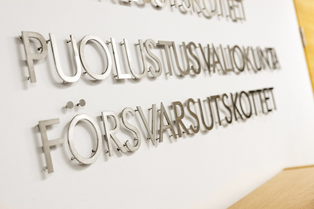 Puolustusvaliokunnan nimi kahdella kielellä metallikirjaimin valkoisella seinällä.